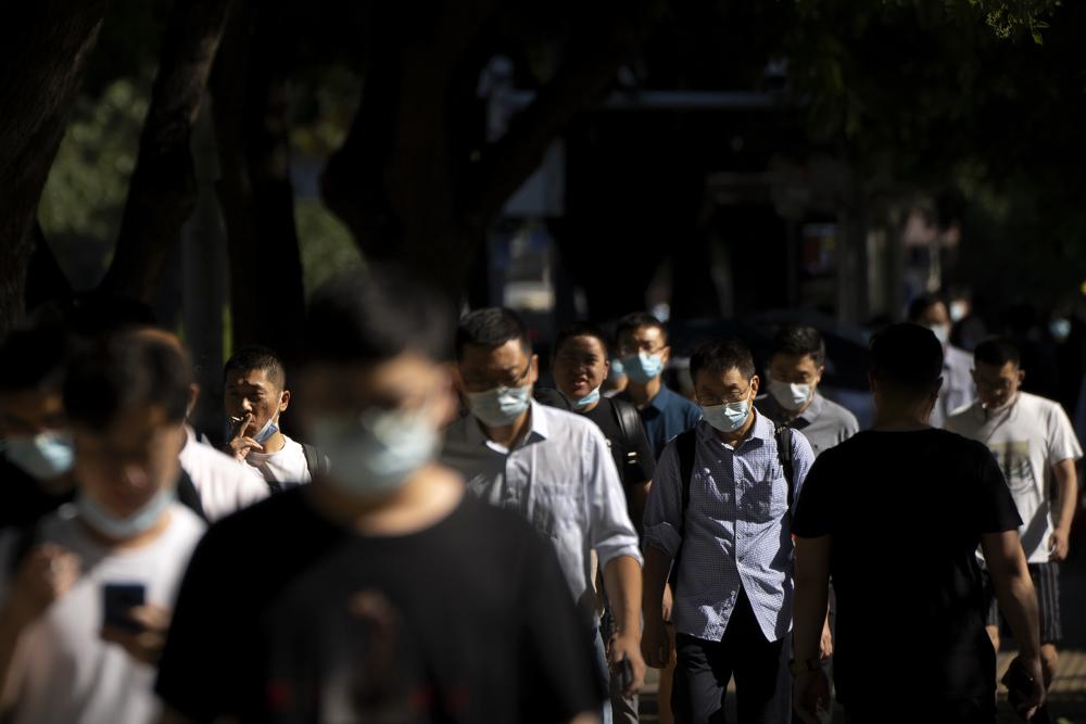 Commuters wearing face masks walk along a street in the central business district in Beijing, Thursday, July 7, 2022. (AP Photo/Mark Schiefelbein)