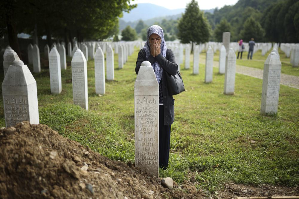 A woman prays near a grave of a family member in the Memorial centre in Potocari, Bosnia, Friday, July 8, 2022. After surviving the 1995 Srebrenica massacre in which over 8,000 of their male relatives were killed, women from the small town in eastern Bosnia dedicated the remaining years of their lives to the re-telling of their trauma to the World, honoring the victims and bringing those responsible for  the killings to justice. (AP Photo/Armin Durgut)