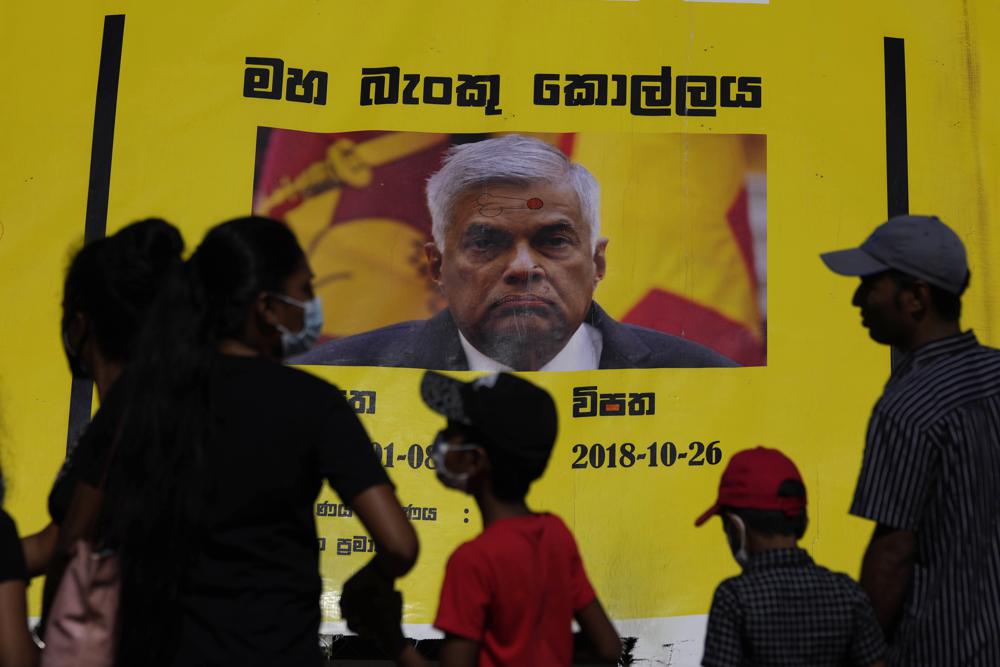 People watch propaganda materials displayed against prime minister Ranil Wickremesinghe outside president Gotabaya Rajapaksa’s office three days after it was stormed by anti government protesters in Colombo, Sri Lanka, Tuesday, July 12, 2022. (AP Photo/Eranga Jayawardena)