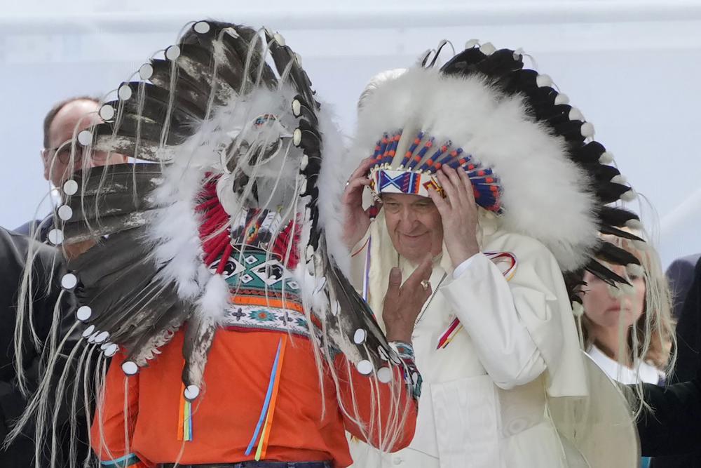 Pope Francis puts on an indigenous headdress during a meeting with indigenous communities, including First Nations, Metis and Inuit, at Our Lady of Seven Sorrows Catholic Church in Maskwacis, near Edmonton, Canada, Monday, July 25, 2022. Pope Francis begins a “penitential” visit to Canada to beg forgiveness from survivors of the country’s residential schools, where Catholic missionaries contributed to the “cultural genocide” of generations of Indigenous children by trying to stamp out their languages, cultures and traditions. Francis set to visit the cemetery at the former residential school in Maskwacis. (AP Photo/Gregorio Borgia)