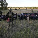In this photo provided by the Serbian Minstry of Interior, a group of migrants detained by Serbian gendarme officers put their hands on their heads, near Subotica, Northern Serbia, Wednesday, July 13, 2022. Authorities in Serbia have detained 85 migrants near the border with Hungary, where a clash earlier this month apparently involving people smugglers left one person dead and several injured. (Serbian Ministry of Interior via AP)