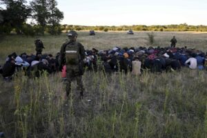 In this photo provided by the Serbian Minstry of Interior, a group of migrants detained by Serbian gendarme officers put their hands on their heads, near Subotica, Northern Serbia, Wednesday, July 13, 2022. Authorities in Serbia have detained 85 migrants near the border with Hungary, where a clash earlier this month apparently involving people smugglers left one person dead and several injured. (Serbian Ministry of Interior via AP)