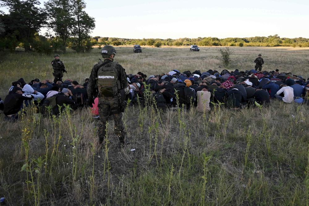 In this photo provided by the Serbian Minstry of Interior, a group of migrants detained by Serbian gendarme officers put their hands on their heads, near Subotica, Northern Serbia, Wednesday, July 13, 2022. Authorities in Serbia have detained 85 migrants near the border with Hungary, where a clash earlier this month apparently involving people smugglers left one person dead and several injured. (Serbian Ministry of Interior via AP)