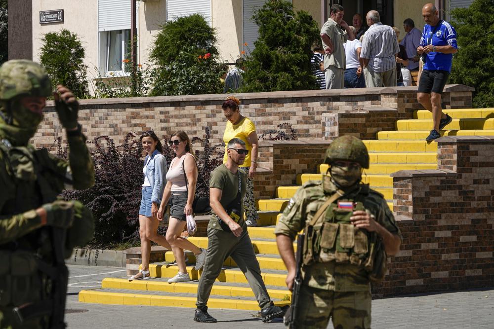 FILE – People walk past as Russian soldiers guard an office for Russian citizenship applications, in Melitopol, south Ukraine, July 14, 2022. Russia took control of part of the Zaporizhzhia region quickly after the launch of the military operation in Ukraine. Ukrainian guerrillas have increasingly challenged the Russian hold on areas in southeastern Ukraine, attacking local Moscow-backed officials, blowing up key infrastructure and spotting targets for the Ukrainian military. This photo was taken during a trip organized by the Russian Ministry of Defense. (AP Photo, File)
