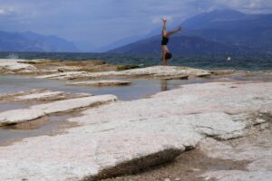A woman takes a roll on the peninsula of Sirmione, on Garda lake, Italy, Friday, Aug. 12, 2022. Lake Garda water level has dropped critically following severe drought resulting in rocks to emerge around the Sirmione Peninsula. (AP Photo/Antonio Calanni)