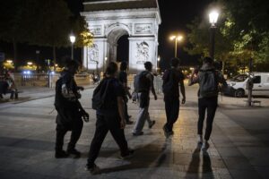 Activists from the collective “On the Spot” walk by the Arc de Triomphe, during a night of action where they will extinguish the lights on dozens of storefronts in Paris, Friday, July 29, 2022. (AP Photo/Lewis Joly)