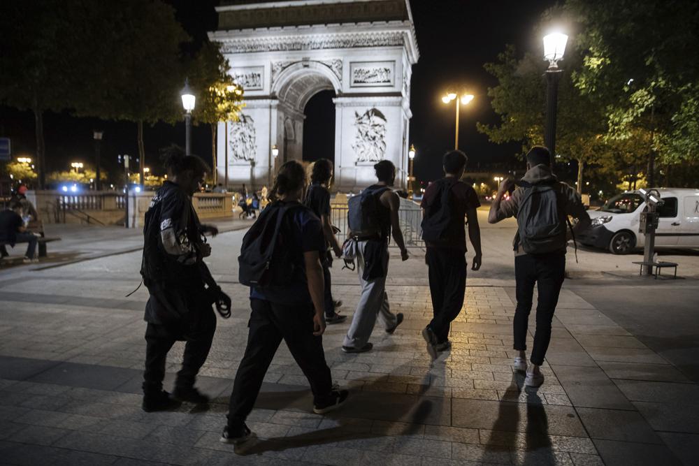 Activists from the collective “On the Spot” walk by the Arc de Triomphe, during a night of action where they will extinguish the lights on dozens of storefronts in Paris, Friday, July 29, 2022. (AP Photo/Lewis Joly)