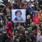 FILE – Supporters of Iran-backed Shiite Coordination Framework attend a rally to denounce their rivals, followers of an influential Shiite cleric Muqtada al-Sadr who stormed the parliament last month and have since been holding a sit-in outside the assembly building in Baghdad, Iraq, Friday, Aug. 12, 2022. On the photo is a revered Shiite Grand Ayatollah Ali al-Sistani. (AP Photo/Anmar Khalil, File)