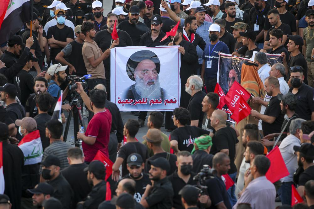 FILE – Supporters of Iran-backed Shiite Coordination Framework attend a rally to denounce their rivals, followers of an influential Shiite cleric Muqtada al-Sadr who stormed the parliament last month and have since been holding a sit-in outside the assembly building in Baghdad, Iraq, Friday, Aug. 12, 2022. On the photo is a revered Shiite Grand Ayatollah Ali al-Sistani. (AP Photo/Anmar Khalil, File)