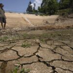 Gan Bingdong stands in the basin of a community reservoir near his farm that ran nearly empty after its retaining wall started to leak and hot weather and drought conditions accelerated the loss of water, in Longquan village in southwestern China’s Chongqing Municipality, Saturday, Aug. 20, 2022. Drought conditions across a swathe of China from the densely populated east across central farming provinces into eastern Tibet have “significantly increased,” the national weather agency said Saturday. The forecast called for no rain and high temperatures for at least three more days from Jiangsu and Anhui provinces northwest of Shanghai, through Chongqing and Sichuan in the southwest to the eastern part of Tibet. (AP Photo/Mark Schiefelbein)