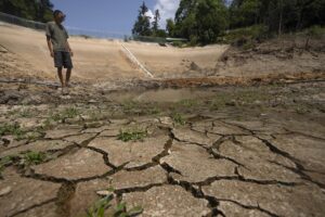 Gan Bingdong stands in the basin of a community reservoir near his farm that ran nearly empty after its retaining wall started to leak and hot weather and drought conditions accelerated the loss of water, in Longquan village in southwestern China’s Chongqing Municipality, Saturday, Aug. 20, 2022. Drought conditions across a swathe of China from the densely populated east across central farming provinces into eastern Tibet have “significantly increased,” the national weather agency said Saturday. The forecast called for no rain and high temperatures for at least three more days from Jiangsu and Anhui provinces northwest of Shanghai, through Chongqing and Sichuan in the southwest to the eastern part of Tibet. (AP Photo/Mark Schiefelbein)