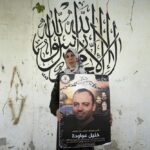 Palestinian Dalal Awawdeh poses with a poster of her husband Khalil Awawdeh, who is a prisoner in Israel, at the family house, in the West Bank village of Idna, Hebron, Tuesday, Aug. 9, 2022. Awawdeh, who is on a protracted hunger strike, was moved Thursday from an Israeli jail to a hospital because of his worsening condition, the prisoner’s wife said. Arabic in the background reads “There is no God but Allah, Muhammad is the Messenger of Allah.” (AP Photo/Nasser Nasser)