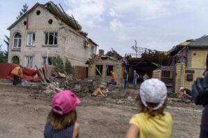 Children watch as workers clean up after a rocket strike on a house in Kramatorsk, Donetsk region, eastern Ukraine, Friday, Aug. 12, 2022. There were no injuries reported in the strike. (AP Photo/David Goldman)