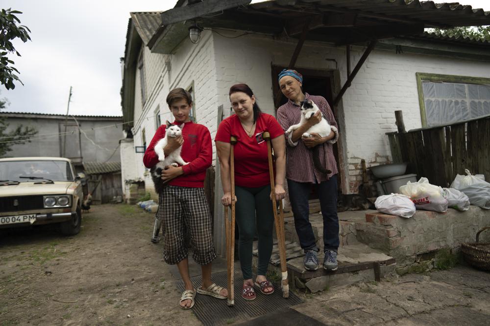 Danyk Rak, 12, his mother Liudmila Koval, centre, and grandmother Nina stand in the village of Voznesenske, near Chernihiv, Ukraine, Saturday, Aug. 13, 2022. Danyk’s family home was destroyed and his mother seriously wounded as Russian forces bombarded Kyiv’s suburbs and surrounding towns in a failed effort to seize the capital. (AP Photo/Evgeniy Maloletka)