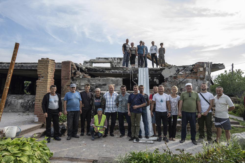 Volunteers pose for a group photo in front of of Zhanna and Serhiy Dynaeva’s house which was destroyed by Russian bombardment, in the village of Novoselivka, near Chernihiv, Ukraine, Saturday, Aug. 13, 2022. Residents in many heavily-damaged areas in Ukraine have set up their own initiatives to rebuild homes before the winter as international organizations rush aid to Ukraine to help with the reconstruction effort. (AP Photo/Evgeniy Maloletka)
