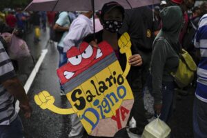 FILE – A teacher holds a sign that reads in Spanish: “Living wage now!” during a pro-government protest by public workers demanding the government pay their full benefits and respect collective bargaining agreements in Caracas, Venezuela, Wednesday, Aug. 10, 2022. (AP Photo/Matias Delacroix, File)