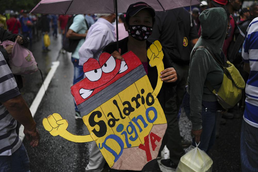 FILE – A teacher holds a sign that reads in Spanish: “Living wage now!” during a pro-government protest by public workers demanding the government pay their full benefits and respect collective bargaining agreements in Caracas, Venezuela, Wednesday, Aug. 10, 2022. (AP Photo/Matias Delacroix, File)