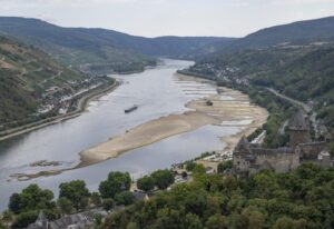 A barge passes exposed rocks and sandbanks on the river Rhine in Bacharach, Germany, Monday, Aug. 15, 2022. After weeks of drought, the water levels of the Rhine have reached historic lows. If the water levels continue to fall, shipping is in danger of coming to a standstill. (Boris Roessler/dpa via AP)