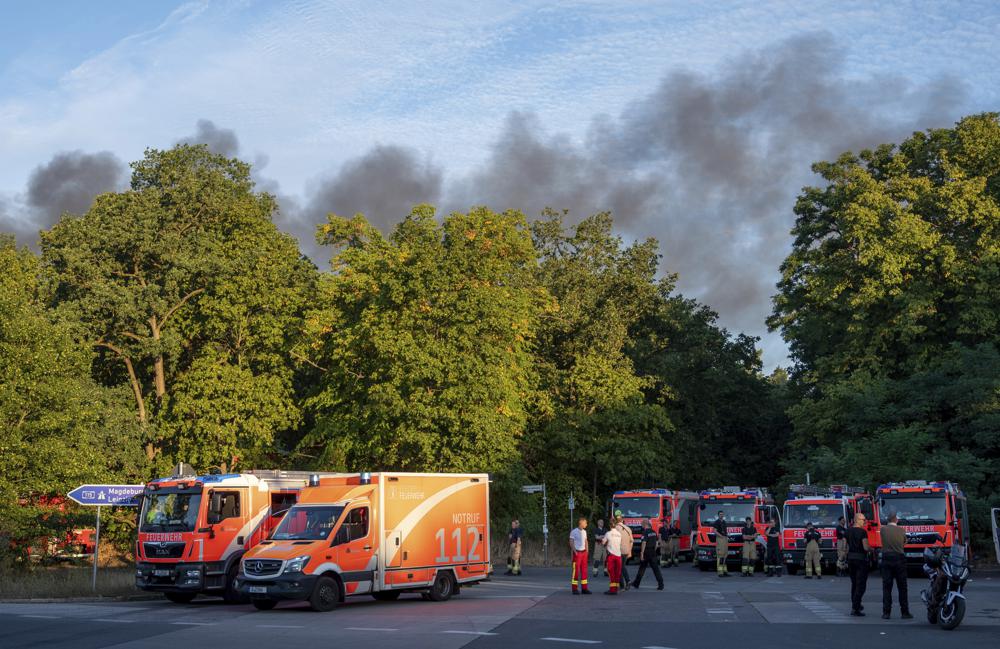 Fire engines and ambulances stand on Kronprinzessinnen road at the Grunewald forest in Berlin, Germany, Thursday, Aug. 4, 2022. A large fire has broke out in one of Berlin’s biggest forests triggered by several explosions that took place on a blasting site inside the forest leading to canceled public transportation and the closure of several roads. Christophe Gateau/dpa via AP)