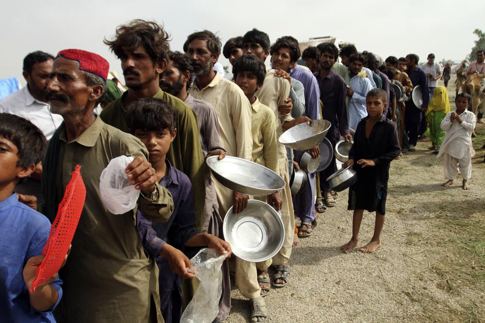 Flood affected people stand in a long line with utensils to get food distributed by Pakistani Army troops in a flood-hit area in Rajanpur, district of Punjab, Pakistan, Saturday, Aug. 27, 2022. Officials say flash floods triggered by heavy monsoon rains across much of Pakistan have killed nearly 1,000 people and displaced thousands more since mid-June. (AP Photo/Asim Tanveer)