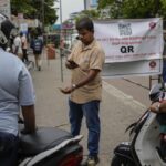 A worker scans a QR code before pumping gas to a vehicle at a fuel station in Colombo, Sri Lanka, Tuesday, Aug. 2, 2022. Sri Lanka introduced fuel distribution using the QR code Monday as part of implementing a weekly quota for motorists. (AP Photo/Eranga Jayawardena)