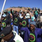 Mine workers sing as they wait for the start of commemoration ceremonies near Marikana in Rustenburg, South Africa, Tuesday, Aug. 16, 2022. South Africa marks on Tuesday 10 years since the Marikana massacre, where 44 people were killed during a mine strike at a platinum mine near Rustenburg, North West province in August 2012. (AP Photo/Themba Hadebe)
