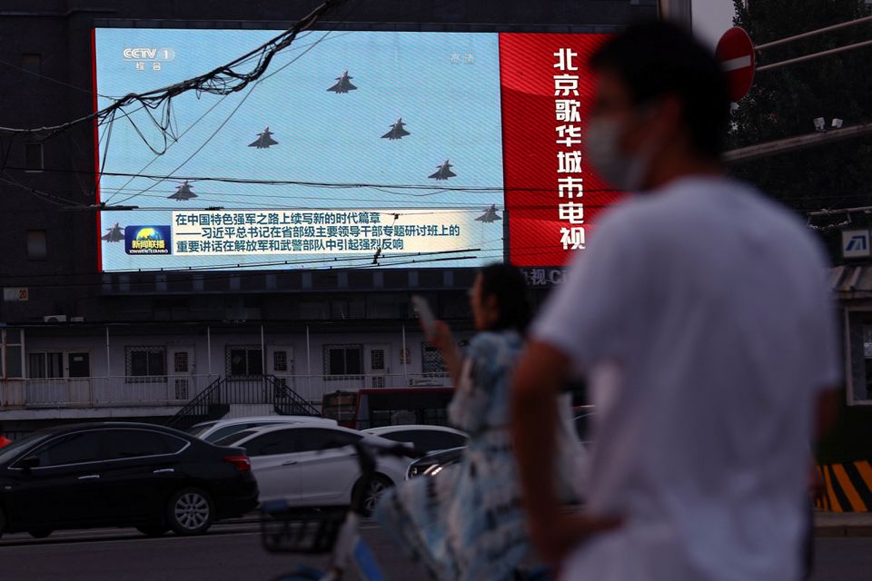 Pedestrians wait at an intersection near a screen showing footage of Chinese People’s Liberation Army (PLA) aircraft during an evening news programme, in Beijing, China August 2, 2022. REUTERS/Tingshu Wang