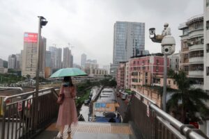 A woman holding an umbrella walks on a pedestrian bridge by surveillance cameras, near Caopu in Shenzhen’s Luohu district, Guangdong province, China July 5, 2022. REUTERS/David Kirton