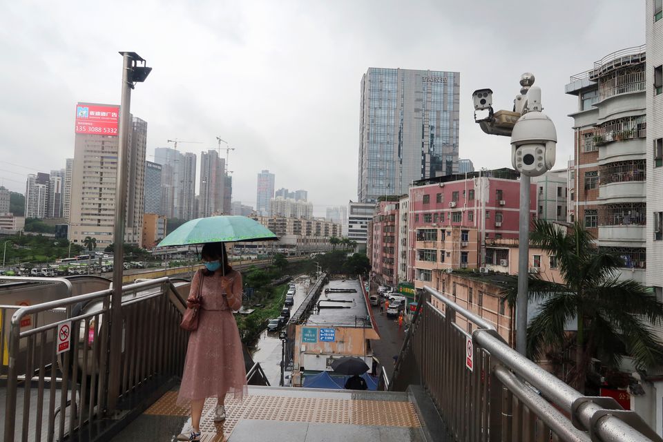 A woman holding an umbrella walks on a pedestrian bridge by surveillance cameras, near Caopu in Shenzhen’s Luohu district, Guangdong province, China July 5, 2022. REUTERS/David Kirton