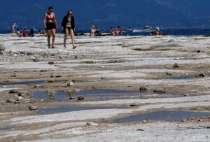 People walk as underwater rocks emerge from the water of Lake Garda after northern Italy experienced the worst drought in 70 years in Sirmione, Italy, August 16, 2022. REUTERS/Flavio Lo Scalzo/File Photo