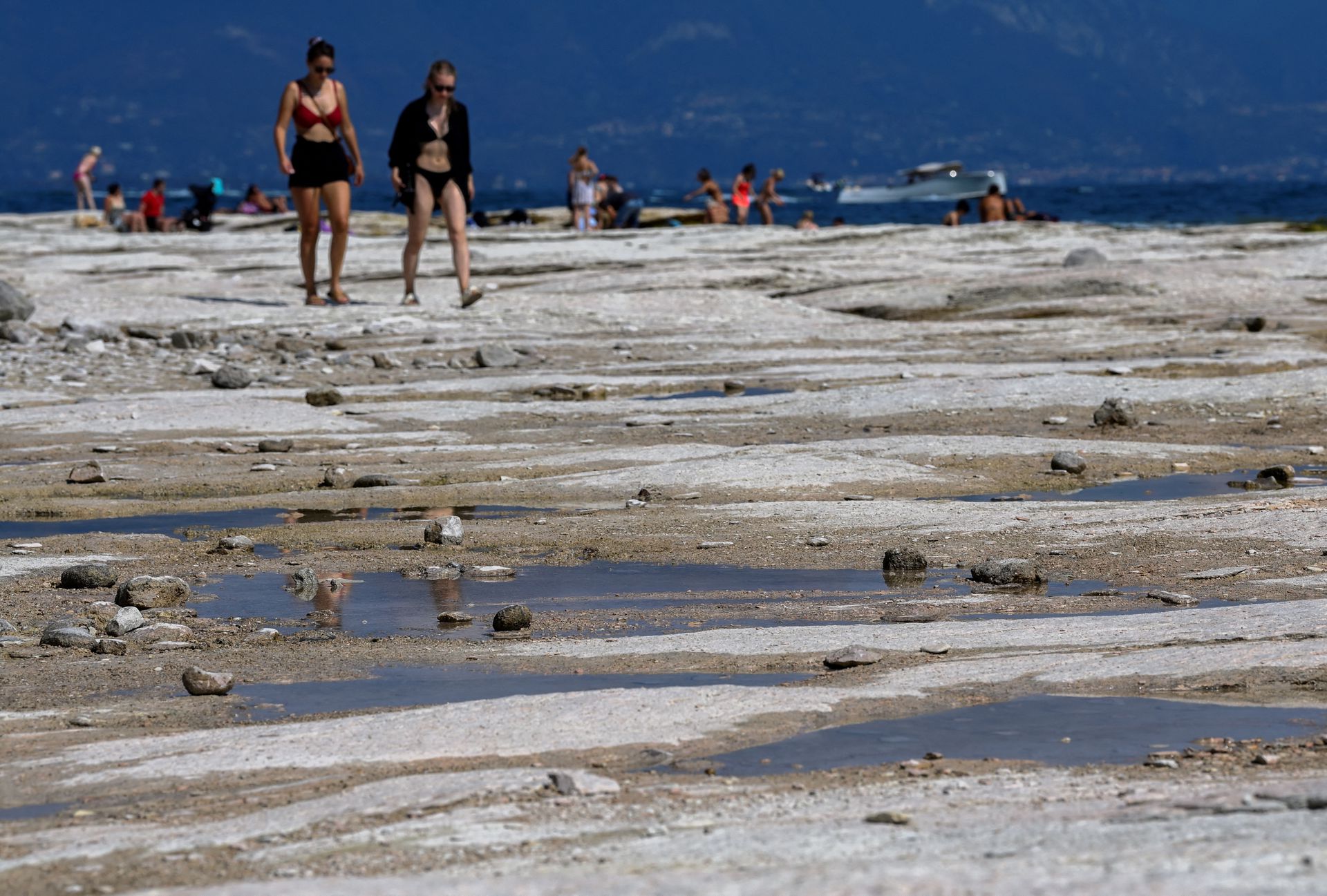 People walk as underwater rocks emerge from the water of Lake Garda after northern Italy experienced the worst drought in 70 years in Sirmione, Italy, August 16, 2022. REUTERS/Flavio Lo Scalzo/File Photo