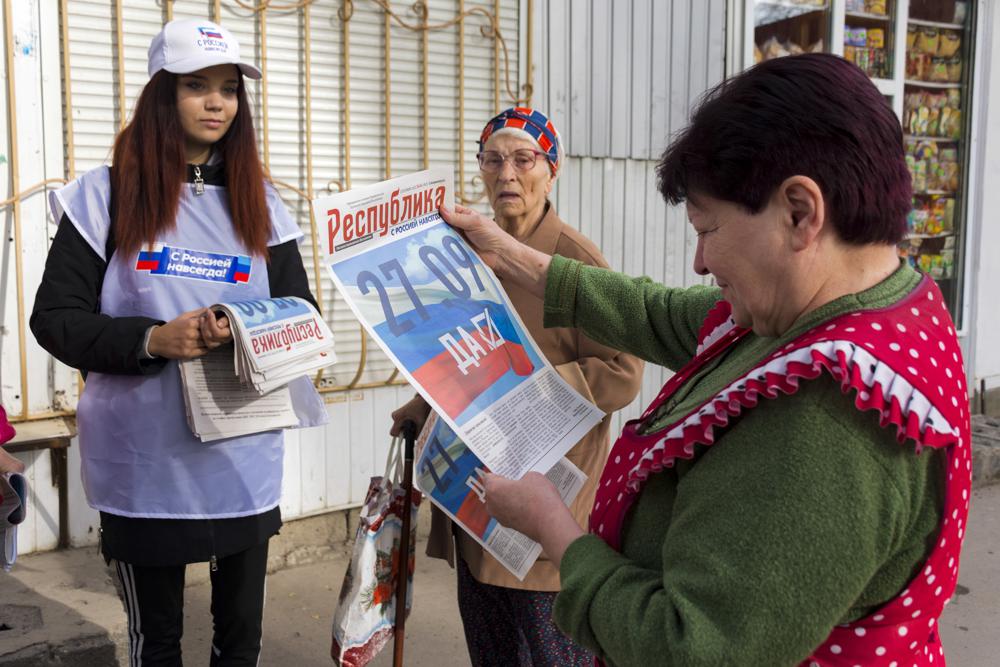 A volunteer of Luhansk regional election commission distributes newspapers to local citizens prior to a referendum in Luhansk, Luhansk People’s Republic controlled by Russia-backed separatists, eastern Ukraine, Thursday, Sept. 22, 2022. Authorities in Russian-controlled regions in eastern and southern Ukraine are preparing to hold referendums on becoming part of Russia — a move that could allow Moscow to escalate the war. The votes start Friday in the Luhansk, Kherson and partly Russian-controlled Zaporizhzhia and Donetsk regions. Writing on newspaper reads in Russian “27.09 Yes.” (AP Photo)