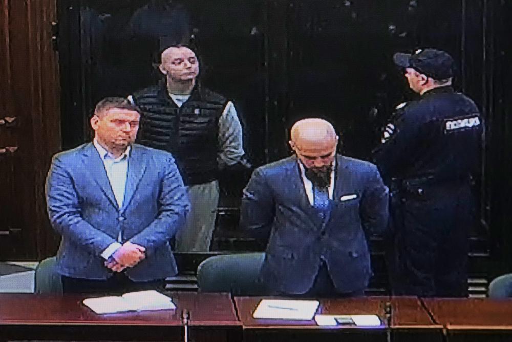 Ivan Safronov, 2nd left, an adviser to the director of Russia’s state space corporation, is seen on a TV screen, as he appears in a video link standing in a cage in a courtroom during sentencing him at the Moscow City Court, in Moscow, Russia, Monday, Sept. 5, 2022. A court in Moscow on Monday found a former journalist Ivan Safronov guilty of treason and sentenced him to 22 years in a maximum security prison, concluding a trial that has been widely seen as politically motivated. (AP Photo/Alexander Zemlianichenko)