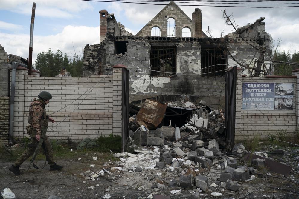 A Ukrainian serviceman from Dnipro-1 regiment walks past a damaged building in the retaken village of Shchurove, Ukraine, Sunday, Sept. 25, 2022. (AP Photo/Leo Correa)