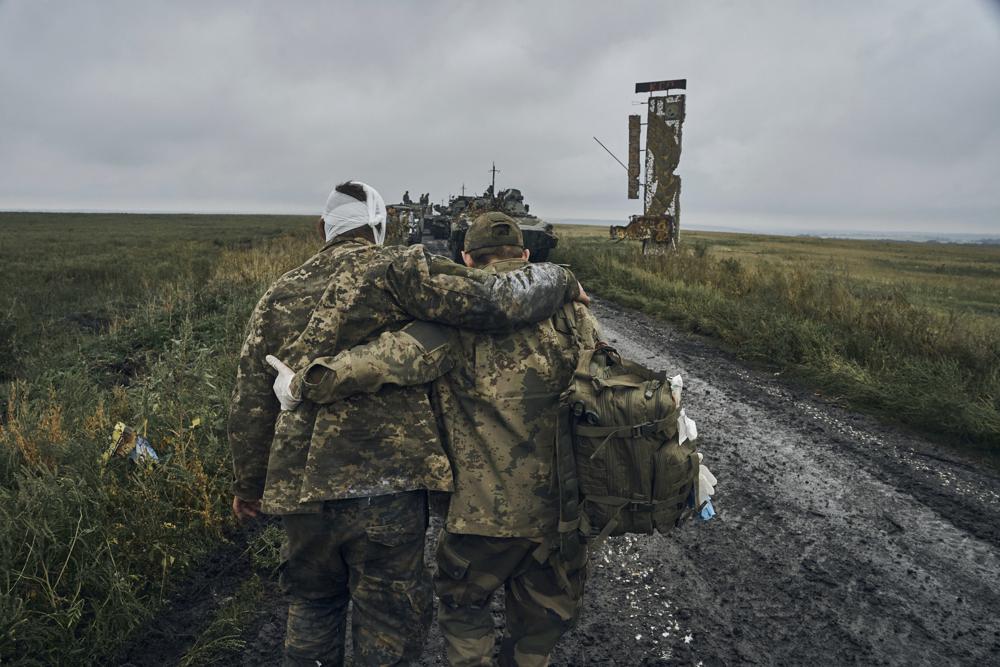 A Ukrainian soldier helps a wounded fellow soldier on the road in the freed territory in the Kharkiv region, Ukraine, Monday, Sept. 12, 2022. Ukrainian troops retook a wide swath of territory from Russia on Monday, pushing all the way back to the northeastern border in some places, and claimed to have captured many Russian soldiers as part of a lightning advance that forced Moscow to make a hasty retreat. (AP Photo/Kostiantyn Liberov)