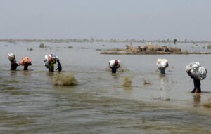 FILE – Victims of heavy flooding from monsoon rains crowd carry relief aid through flood water in the Qambar Shahdadkot district of Sindh Province, Pakistan, Sept. 9, 2022. The United Nations says weather disasters costing $200 million a day and irreversible climate catastrophe looming show the world is “heading in the wrong direction.” (AP Photo/Fareed Khan, File)