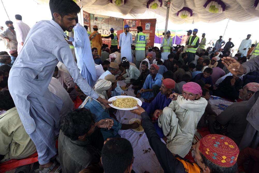 Victims of the unprecedented flooding from monsoon rains receive relief food organized by the Alkhidmat Foundation, in Jaffarabad, a district of Pakistan’s southwestern Baluchistan province, Monday, Sept. 5, 2022. The U.N. refugee agency rushed in more desperately needed aid Monday to flood-stricken Pakistan as the nation’s prime minister traveled to the south where rising waters of Lake Manchar pose a new threat. (AP Photo/Fareed Khan)