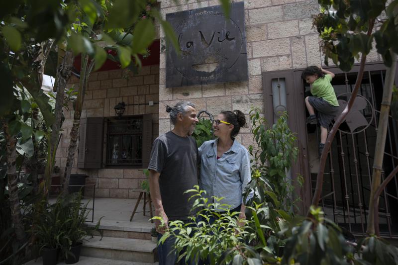 FILE – Kenae Totah, 5, right, plays while his parents Morgan Cooper, 41, center and foreign spouse Saleh Totah, right, pose for a photo in front of their restaurant, at the West Bank city of Ramallah, Monday, May 2, 2022. Israel published a new set of rules and restrictions Sunday, Sept. 4, 2022, for foreigners who want to enter or live in Palestinian areas of the West Bank, including a requirement that people who form romantic relationships with local Palestinians register with Israeli authorities. (AP Photo/Nasser Nasser, File)