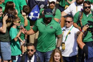 Former Notre Dame player Manti Te’o follows members of the Notre Dame football team walk through the crowd to the stadium before an NCAA college football game against California in South Bend, Ind., Saturday, Sept. 17, 2022. (AP Photo/Michael Conroy)