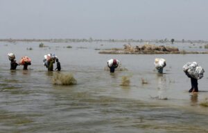 FILE – Victims of heavy flooding from monsoon rains carry relief aid through flood water in the Qambar Shahdadkot district of Sindh Province, Pakistan, Sept. 9, 2022. Scientists have said climate change no doubt helped swell monsoon rains this summer that dumped three and a half times the normal amount of rain, putting a third of Pakistan underwater. The destruction has intensified the debate over a question of climate justice: Whether rich countries whose emissions have been the main driver of climate change owe compensation for the damage that change is inflicting on poor countries.(AP Photo/Fareed Khan, File)