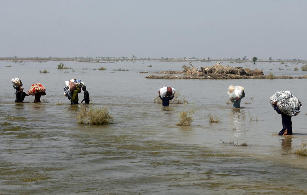 FILE – Victims of heavy flooding from monsoon rains carry relief aid through flood water in the Qambar Shahdadkot district of Sindh Province, Pakistan, Sept. 9, 2022. Scientists have said climate change no doubt helped swell monsoon rains this summer that dumped three and a half times the normal amount of rain, putting a third of Pakistan underwater. The destruction has intensified the debate over a question of climate justice: Whether rich countries whose emissions have been the main driver of climate change owe compensation for the damage that change is inflicting on poor countries.(AP Photo/Fareed Khan, File)