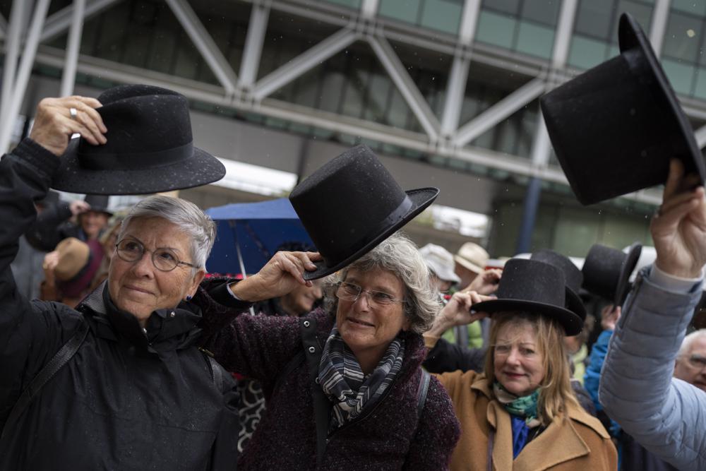 Campaigners take their hat off in a show of respect for people who took their own lives in The Hague, Netherlands, Monday, Oct. 10, 2022, where they calling for the decriminalization of assisted suicide in the Netherlands took the Dutch state to court, arguing its ban breaches human rights norms. The case at The Hague District Court was brought by a group called Cooperative Last Will, which has long urged a change of the law to allow people to help relatives end their lives. (AP Photo/Peter Dejong)