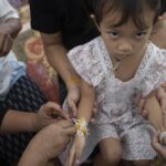 Relatives of the victims of the mass killing attack tie holy threads on the wrists of 3 year old Paweenuch Supolwong, the only child to emerge unscathed, inside Wat Rat Samakee temple in Uthai Sawan, north eastern Thailand, Saturday, Oct. 8, 2022. A former police officer burst into a day care center in northeastern Thailand on Thursday, killing dozens of preschoolers and teachers before shooting more people as he fled. (AP Photo/Wason Wanichakorn)