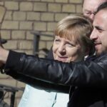 FILE – In this Sept. 10, 2015, file photo, refugee Rodin Saouan from Syria takes a picture of himself and German Chancellor Angela Merkel, left, during Merkel’s visit at a registration center for migrants and refugees in Berlin, Germany. The U.N. refugee agency says it’s giving its highest award to former German Chancellor Angela Merkel for her efforts to bring in more than 1 million refugees — mostly from Syria — into Germany, despite some pockets of criticism at both home and abroad. (AP Photo/Michael Sohn, File)