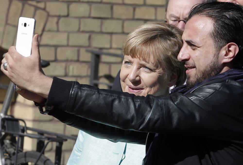 FILE – In this Sept. 10, 2015, file photo, refugee Rodin Saouan from Syria takes a picture of himself and German Chancellor Angela Merkel, left, during Merkel’s visit at a registration center for migrants and refugees in Berlin, Germany. The U.N. refugee agency says it’s giving its highest award to former German Chancellor Angela Merkel for her efforts to bring in more than 1 million refugees — mostly from Syria — into Germany, despite some pockets of criticism at both home and abroad. (AP Photo/Michael Sohn, File)