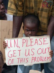FILE- A Liberian child holds a sign pleading the United Nations to allow Liberians to leave the war-torn country of Liberia while standing on the quay of Monrovia’s port, Friday May 17, 1996. A former Liberian rebel is going on trial Monday, Oct. 10, 2022, in Paris, on charges of crimes against humanity, torture and acts of barbarism during the West African country’s civil war in the 1990s. (AP Photo/Jean-Marc Bouju, File)
