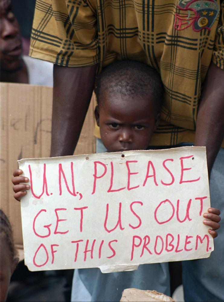 FILE- A Liberian child holds a sign pleading the United Nations to allow Liberians to leave the war-torn country of Liberia while standing on the quay of Monrovia’s port, Friday May 17, 1996. A former Liberian rebel is going on trial Monday, Oct. 10, 2022, in Paris, on charges of crimes against humanity, torture and acts of barbarism during the West African country’s civil war in the 1990s. (AP Photo/Jean-Marc Bouju, File)