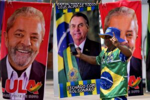A demonstrator dressed in the colors of the Brazilian flag performs in front of a street vendor’s towels for sale featuring Brazilian presidential candidates, current President Jair Bolsonaro, center, and former President Luiz Inacio Lula da Silva, in Brasilia, Brazil, Tuesday, Sept. 27, 2022. Nearly a dozen candidates are running in Brazil’s presidential election but only two stand a chance of reaching a runoff: former President Luiz Inacio Lula da Silva and incumbent Jair Bolsonaro. (AP Photo/Eraldo Peres)
