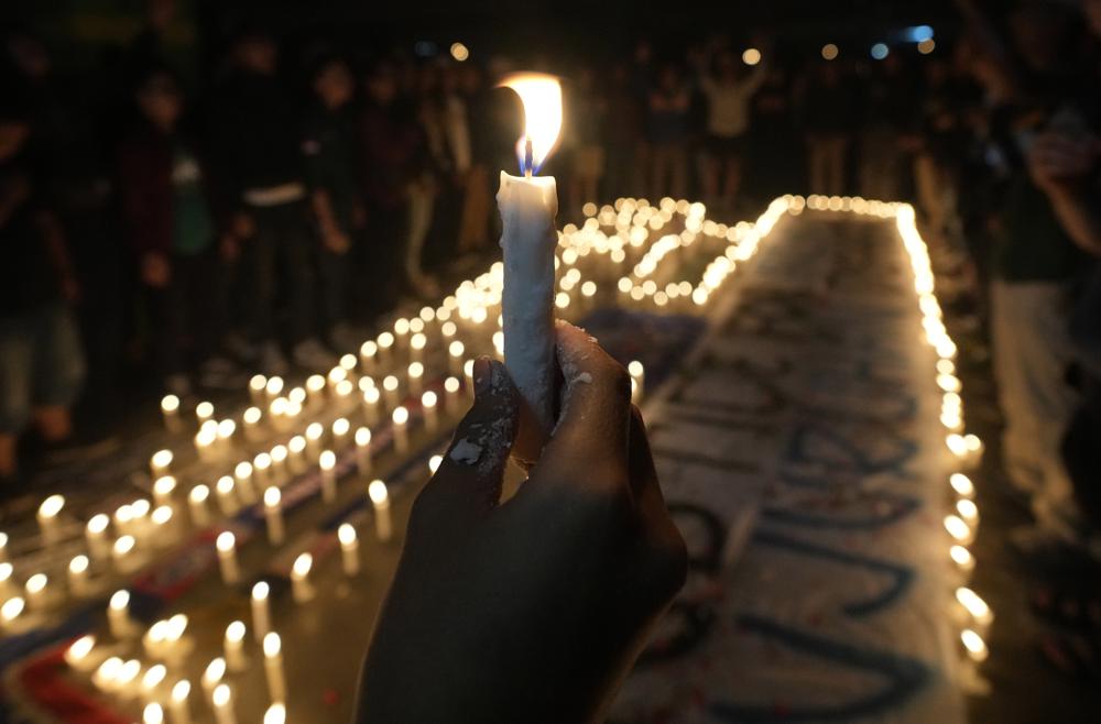 A man holds a candle during a candle light vigil for Arema FC Supporters who died following Saturday’s soccer match stampede, at Patriot Stadium in Bekasi, Indonesia, Monday, Oct. 3, 2022. Indonesian police said they were investigating over a dozen officers responsible for firing tear gas that set off a crush that killed a number of people at a soccer match as families and friends grieved Monday for the victims that included children. (AP Photo/Tatan Syuflana)
