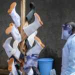A medical attendant stands by rubber boots hung up to dry after being disinfected, outside the Ebola isolation section of Mubende Regional Referral Hospital, in Mubende, Uganda, Thursday, Sept. 29, 2022. In this remote Ugandan community facing its first Ebola outbreak, testing trouble has added to the challenges with symptoms of the Sudan strain of Ebola now circulating being similar to malaria, underscoring the pitfalls health workers face in their response. (AP Photo/Hajarah Nalwadda)